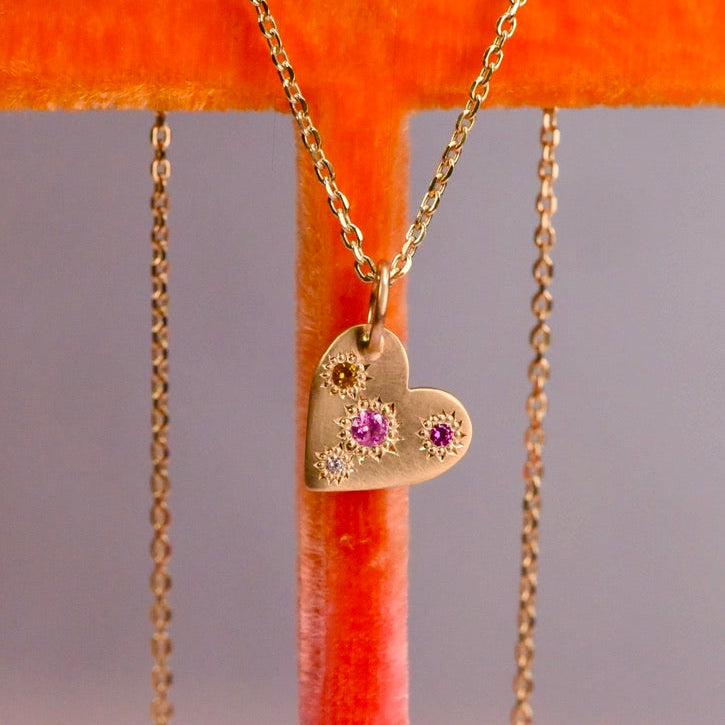 Gold heart-shaped necklace with gemstones on an orange stand.