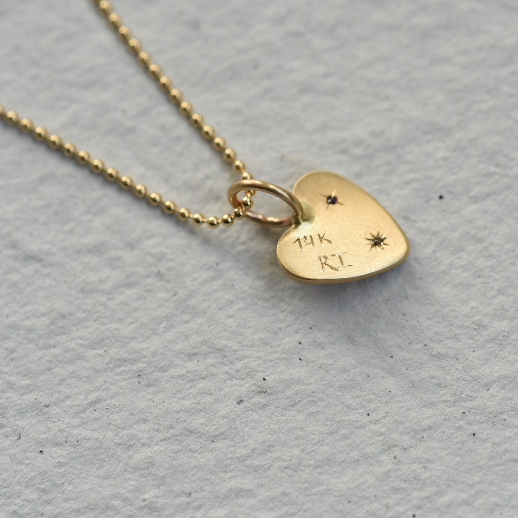 Backside of a gold heart charm, set with sapphires and a diamond. Hand engraved by Corkie Bolton.