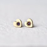 Close-up of Misfit 14k Gold Studs on a white background: A detailed view of the Misfit 14k gold heart-shaped studs, each featuring a color-treated purple sapphire cabochon, showcasing their unique handcrafted design and matte finish.