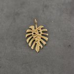 Flat-lay of the Monstera charm: A flat-lay image of the gold Monstera charm on a neutral background, emphasizing the craftsmanship and glossy finish.