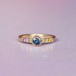 Front view of a one-of-a-kind Montana sapphire ring in 10k yellow gold, featuring a .50ct hand-selected center stone and an ombré of orange, yellow, and pink sapphires in castle settings with milgrain detail.
