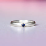 Silver ring with a 14k yellow gold prong set blue sapphire on a gradient pink and purple background