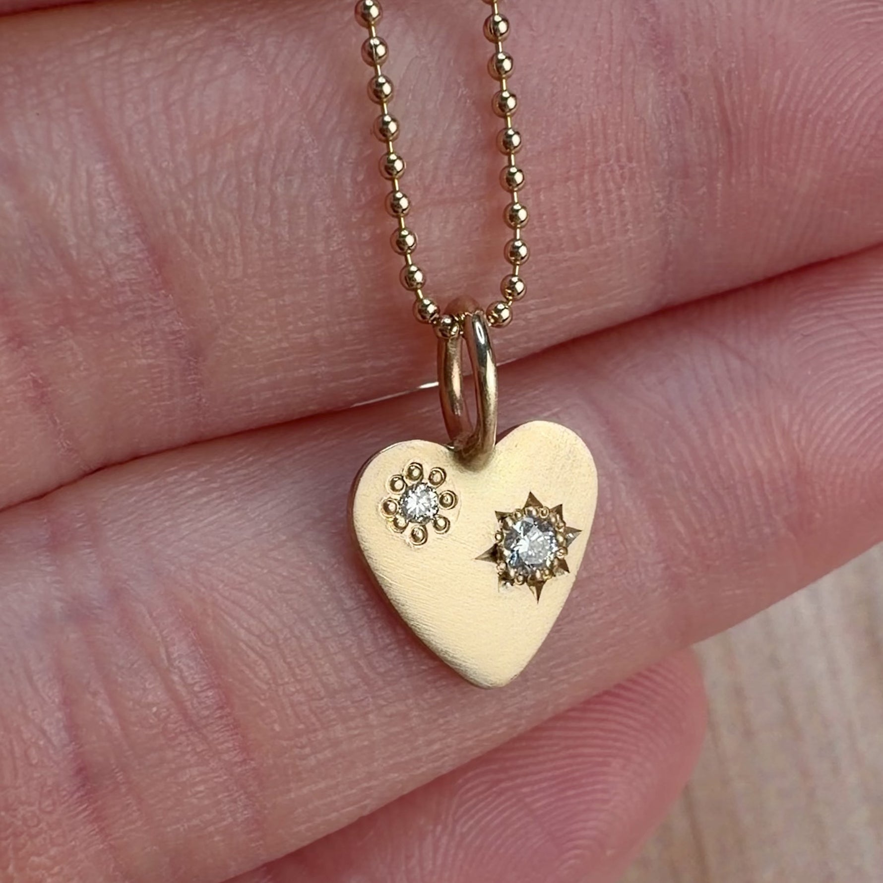 Video of a solid 14k yellow gold hand engraved diamond heart charm on a ball chain.