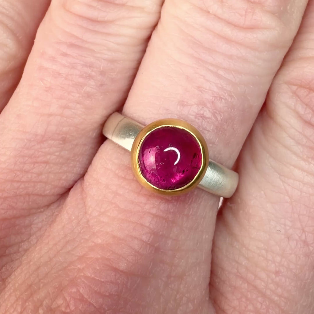 Video of a hand wearing a silver ring with a pink tourmaline cabochon set in 18k yellow gold.