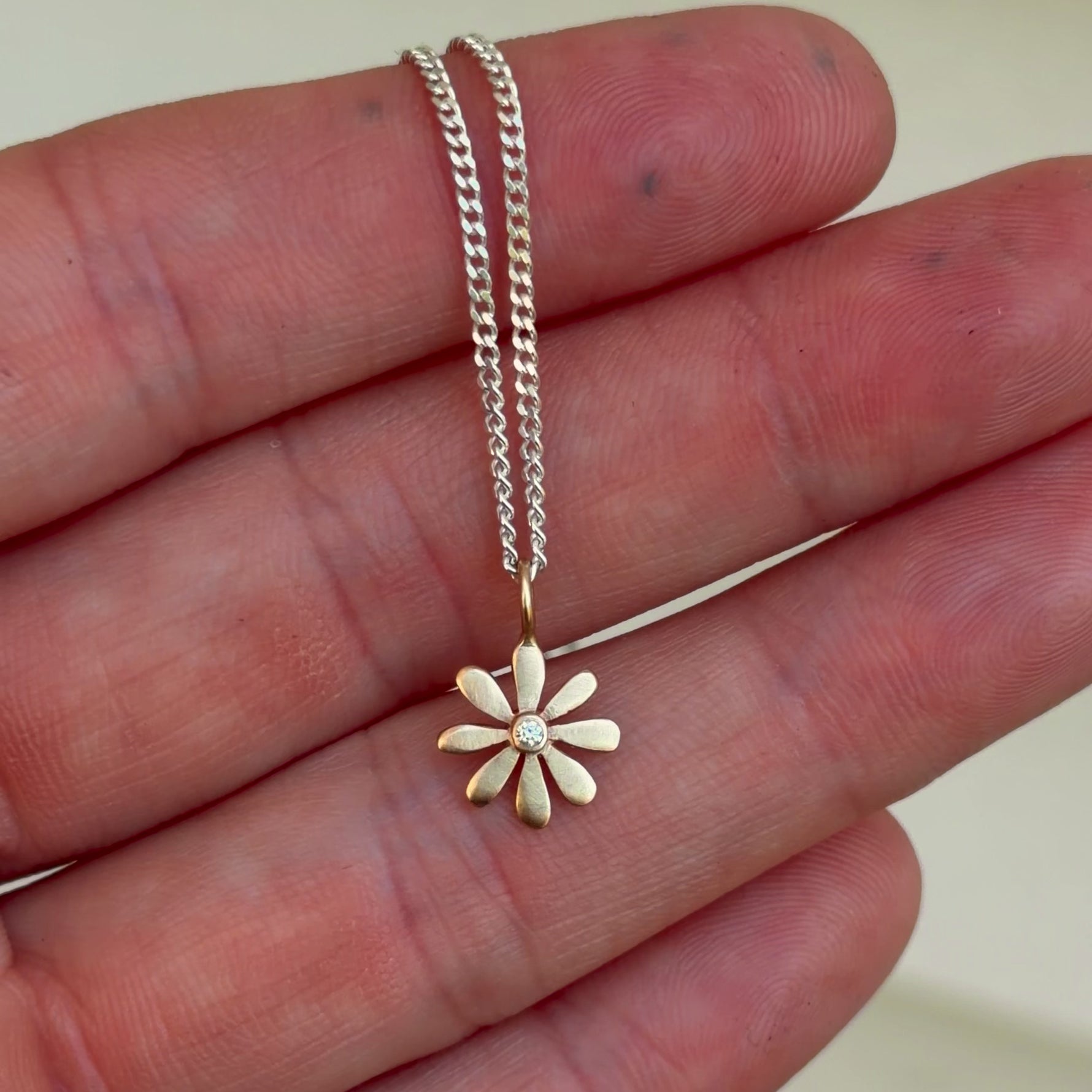 14k gold flower charm with diamond on curb chain in hand.