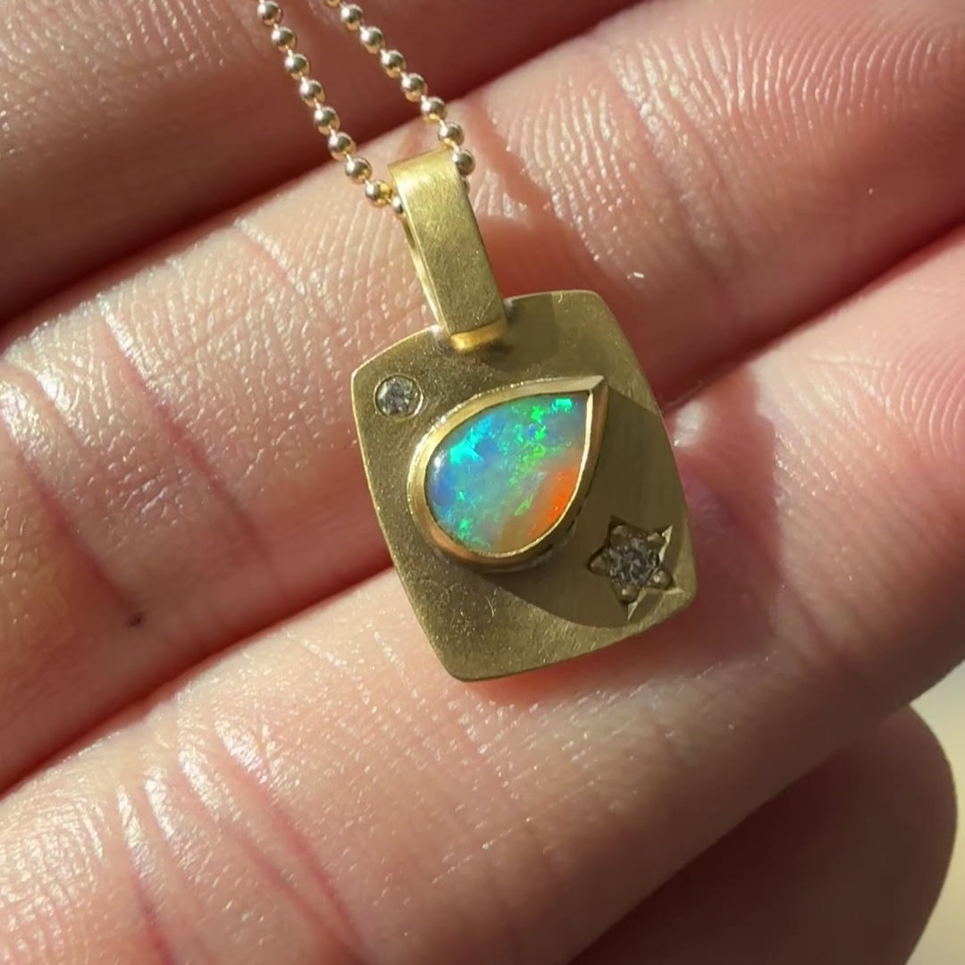 An 18k gold engraved charm with diamonds and an opal in a teardrop shape.