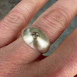 A close-up video still of a chunky brushed sterling silver dome ring with a 14k yellow gold bezel set with a faceted salt and pepper diamond, worn on a finger.