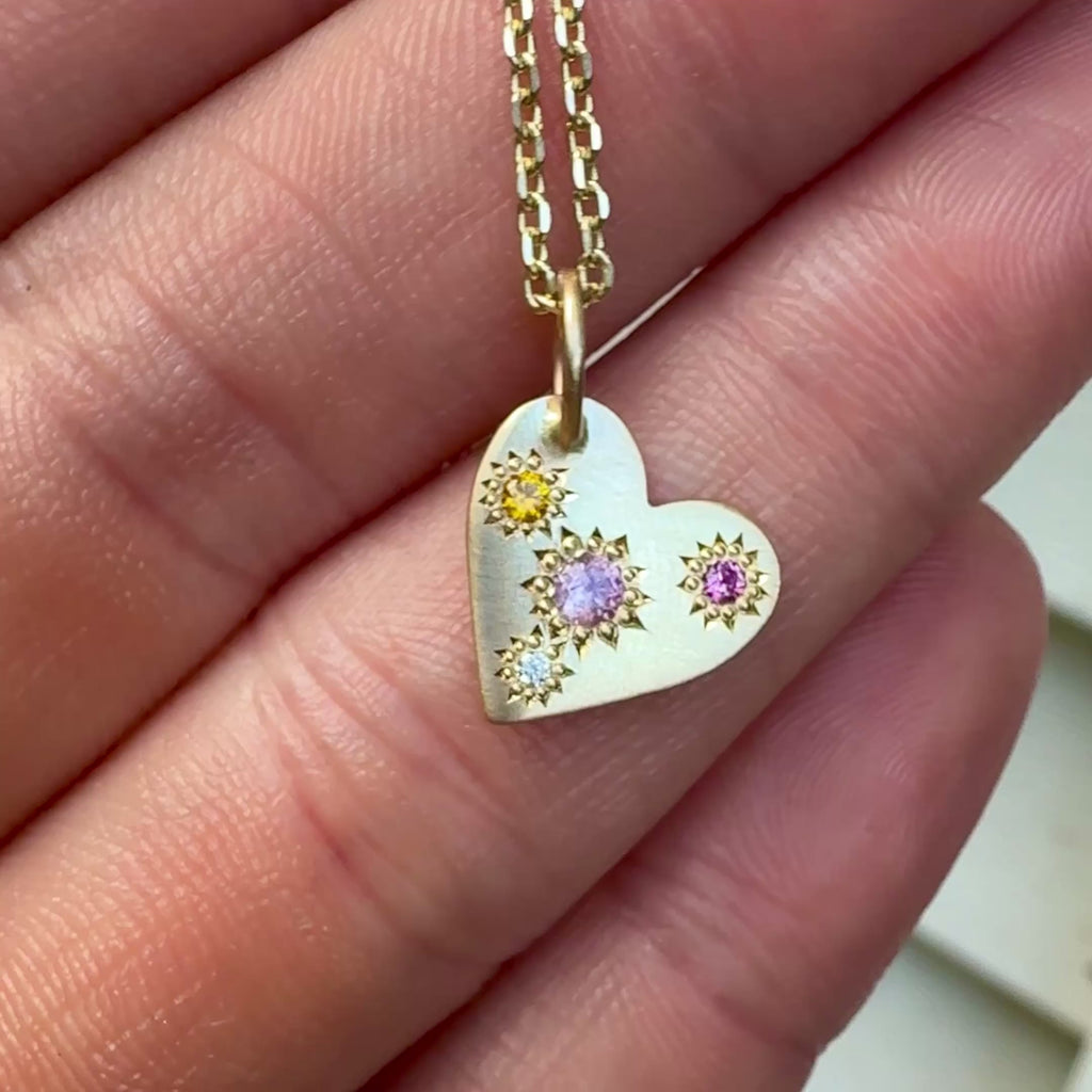 Video of Misfit Pastel Sapphires and Diamond Heart Necklace catching the light, showing asymmetrical star settings and golden shimmer.