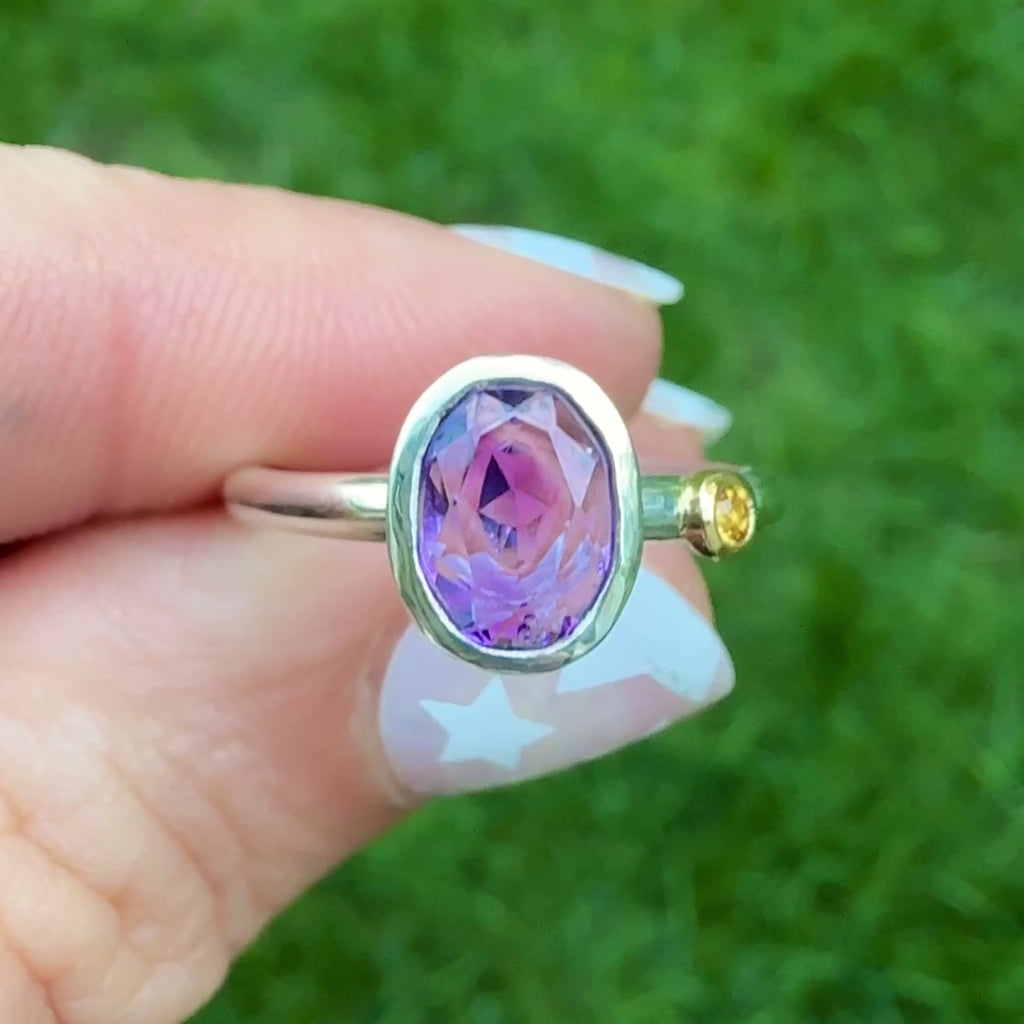 Video of a sterling silver oval amethyst ring with an orange sapphire accent in 14k gold, shown outdoors in natural light.