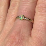 ideo of the Asymmetrical Black Opal + Sapphire 14k Gold Ring by Corkie Bolton Jewelry, capturing the opal’s vivid play of color with flashes of green, blue, and neon orange as the light moves.