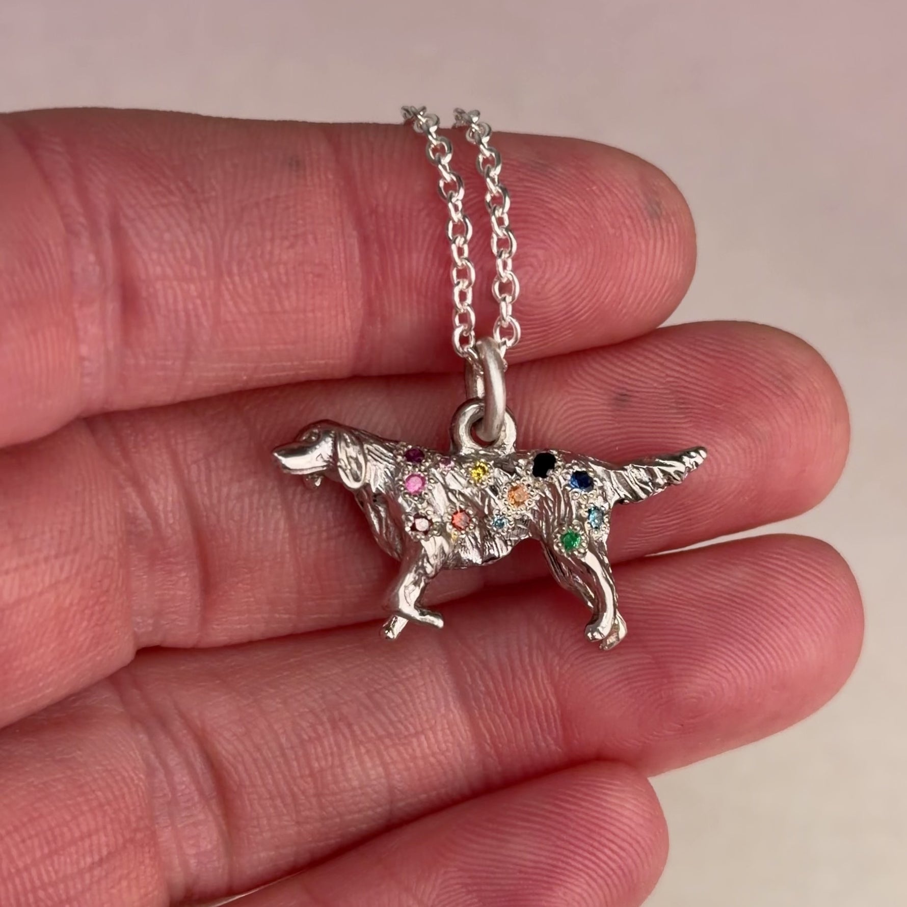 Video of a vintage mid-century sterling silver golden retriever charm with hand engraved star settings flush set with pink, purple, yellow, orange, red, and brown sapphires and colored diamonds held in a hand.