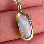 Video of a Lightning Ridge crystal opal pendant bezel set in 22k yellow gold on a sterling silver cable chain showing live play of color