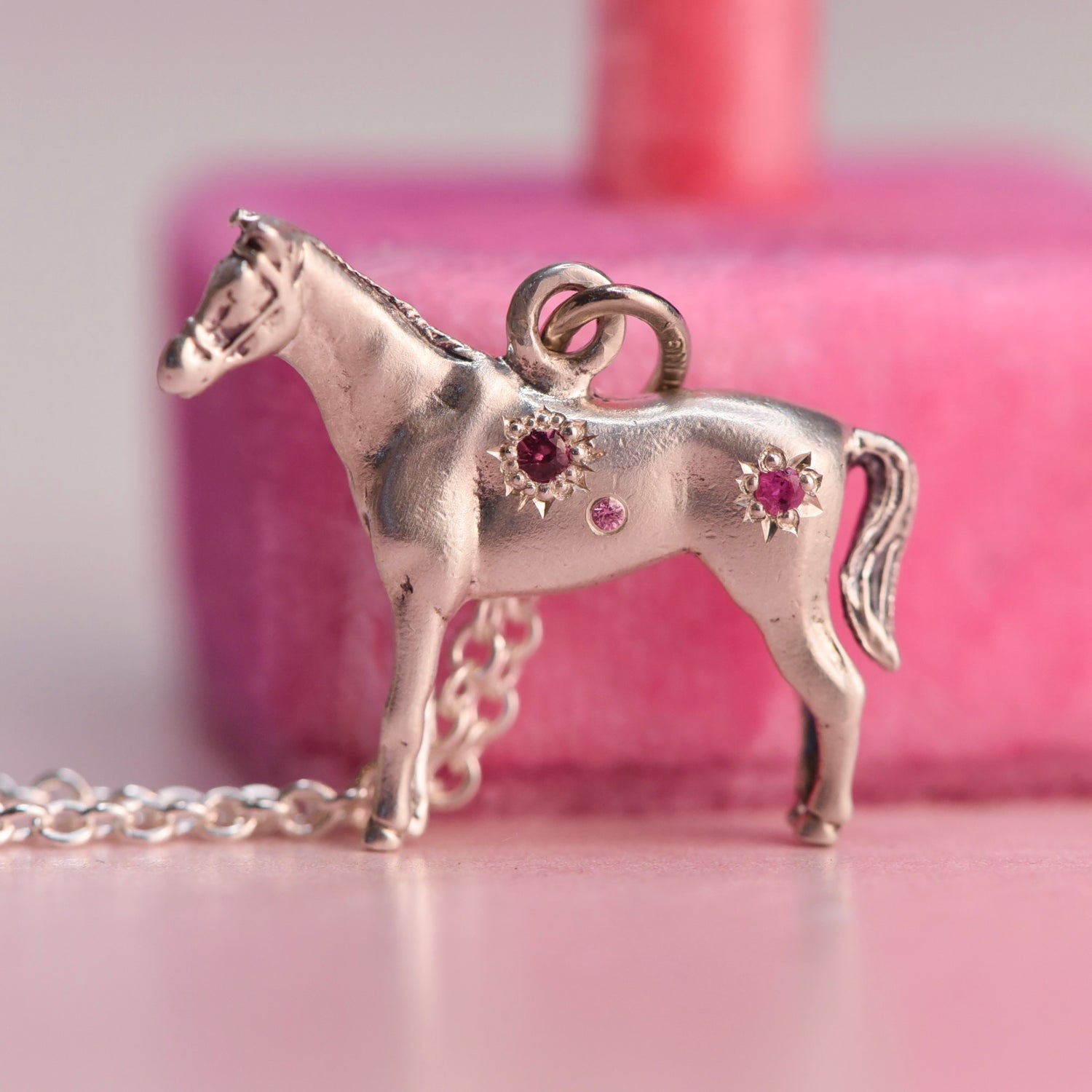 Silver horse-shaped pendant with gemstones on a pink background