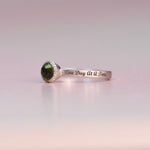 Silver ring with green gemstone and 'One Day At A Time' engraving on a light pink background