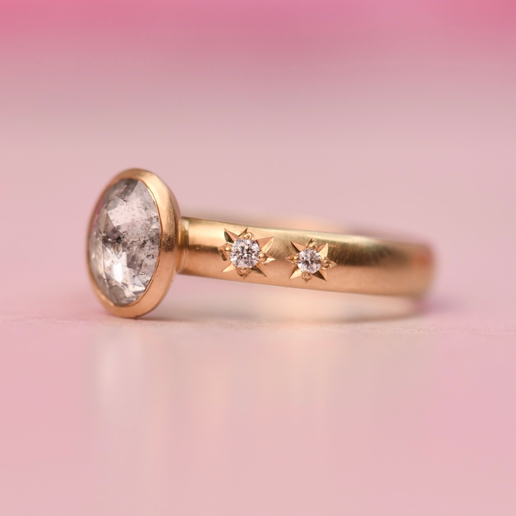 Side profile of an 18k yellow gold engagement ring set with an oval salt and pepper rose cut diamond, showing two accent diamonds in star settings.