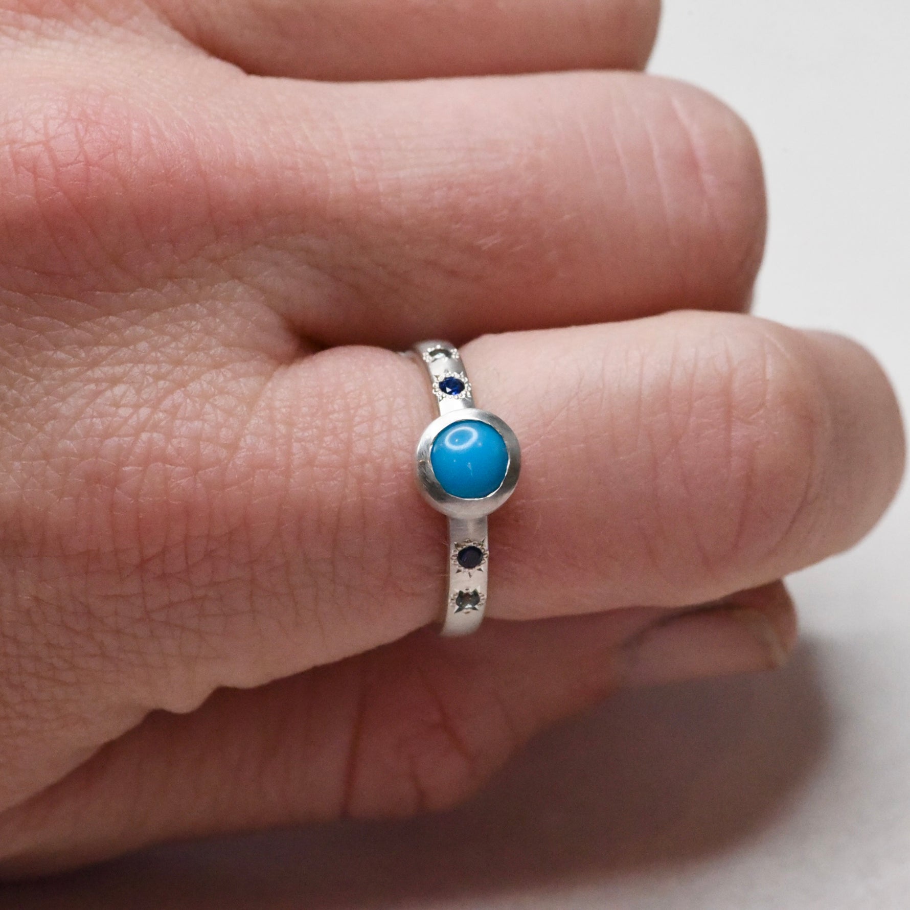 Handmade Sleeping Beauty turquoise and sapphire silver ring shown on hand, highlighting the bezel setting and engraved star accents.