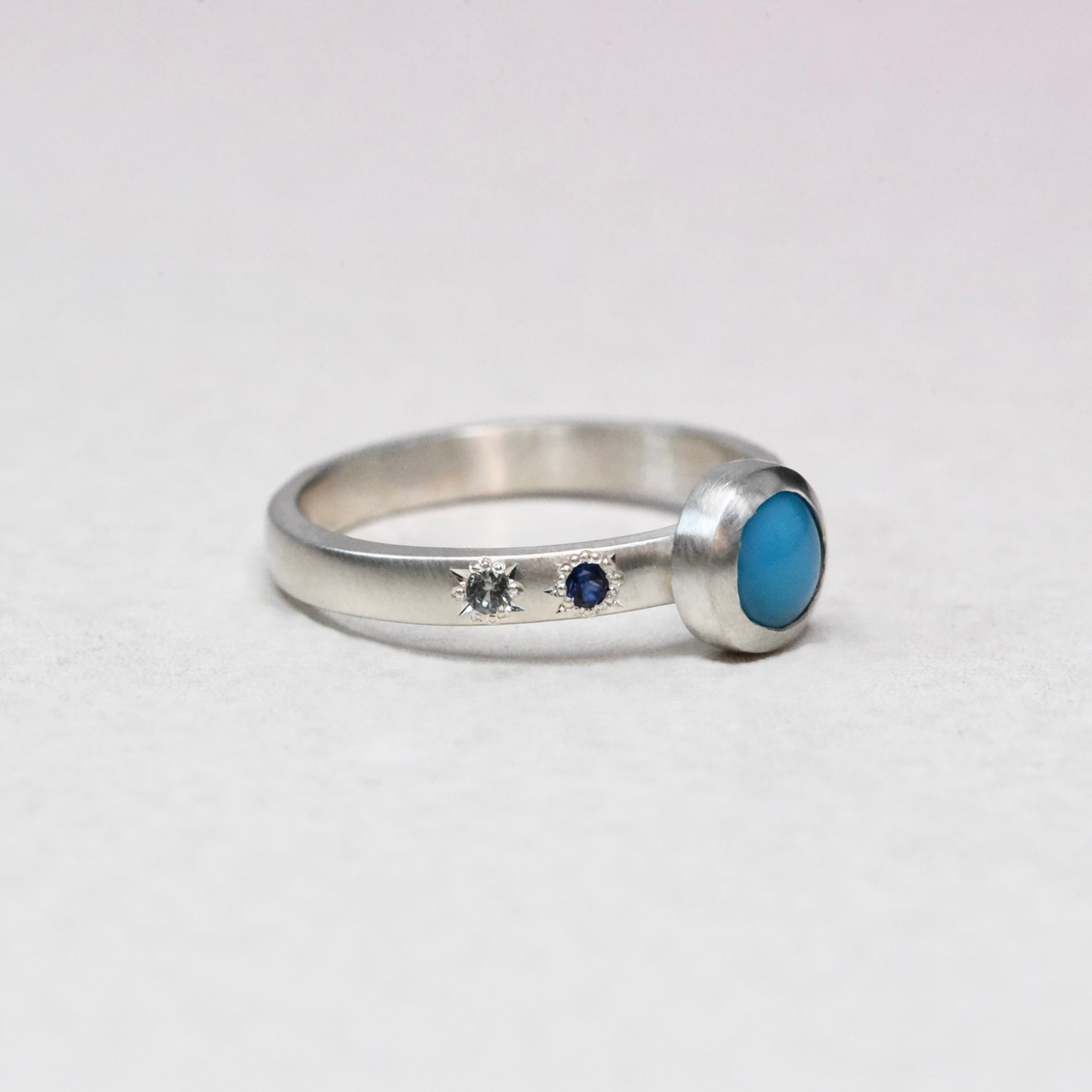 Side angle of the sterling silver Sleeping Beauty turquoise ring showing the thick bezel and hand-engraved star details set with blue sapphires.