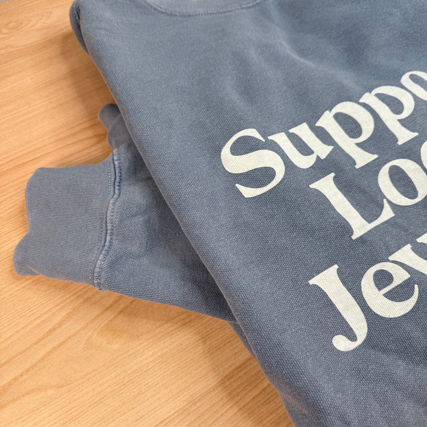 Support Local Jewelers sweatshirt in Blue Jean — a faded denim-blue garment-dyed unisex crewneck with a soft, lived-in feel, by Corkie Bolton Jewelry. Sleeve details.