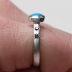 Sterling silver turquoise and sapphire star ring by Corkie Bolton Jewelry shown from a side angle on hand, capturing the depth of the bezel and engraved details.