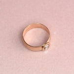 Angled view of a wide 14k yellow gold vintage band ring with an 18k yellow gold hand-engraved bezel set with a 0.40ct salt and pepper rose cut diamond, displayed on a soft blush pink surface.
