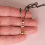 Hand holding a vintage mid-century 18k yellow gold anchor and rope charm necklace with star set white diamond on an oxidized black rolo chain with 14k gold links, by Corkie Bolton Jewelry