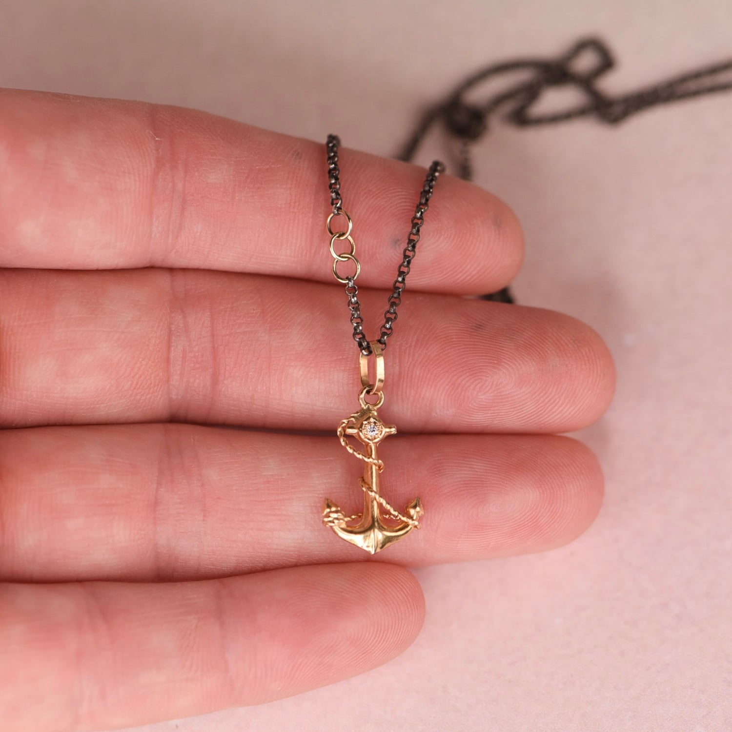 Hand holding a vintage mid-century 18k yellow gold anchor and rope charm necklace with star set white diamond on an oxidized black rolo chain with 14k gold links, by Corkie Bolton Jewelry