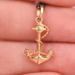 Close up back view of a vintage mid-century 18k yellow gold anchor and rope charm held in fingers showing detailed rope texture, sculpted flukes, and 750 hallmark stamp on the bail, on an oxidized black rolo chain, by Corkie Bolton Jewelry
