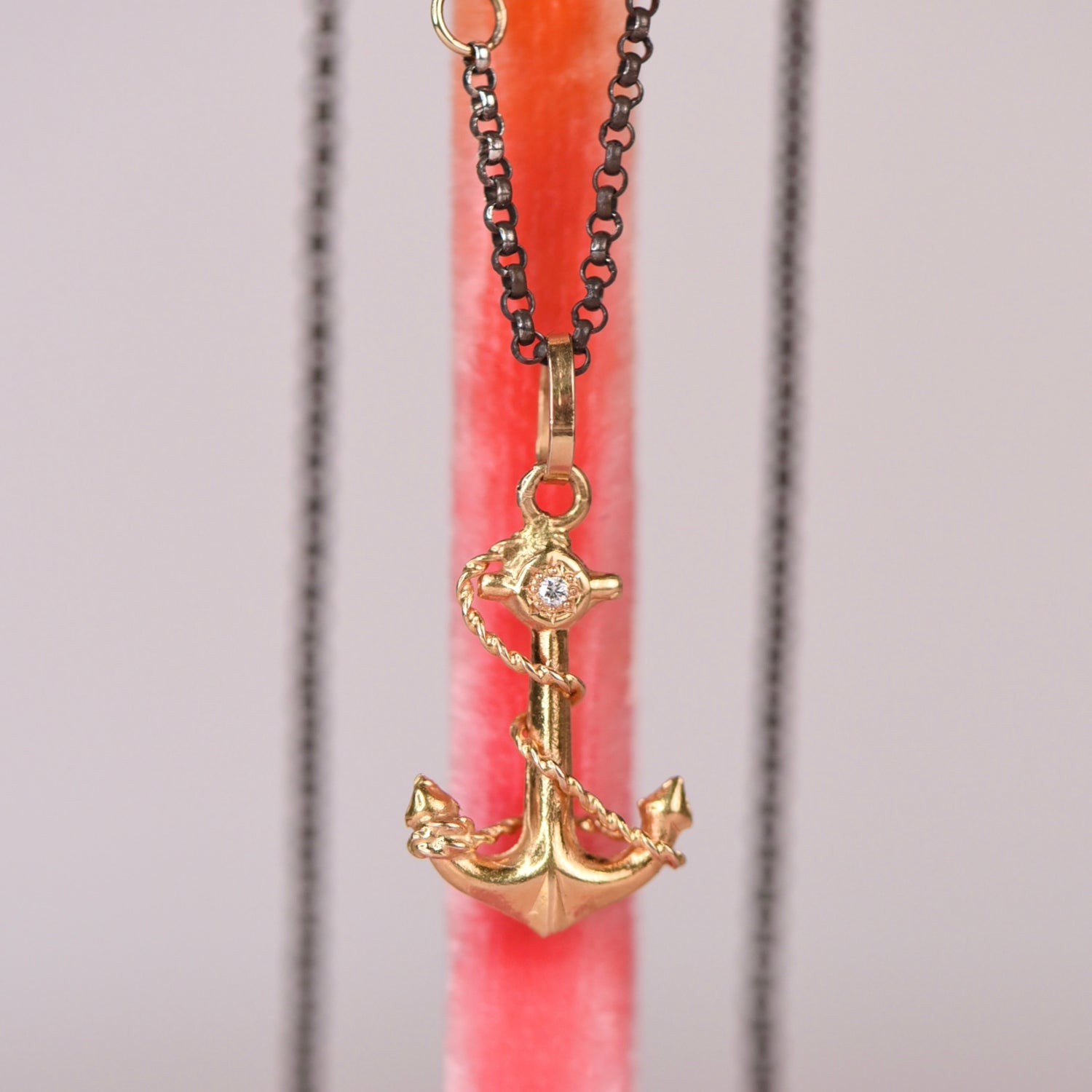 Vintage mid-century 18k yellow gold anchor and rope charm pendant with hand engraved star set white diamond hanging on an oxidized black rolo chain against a pink display stand, by Corkie Bolton Jewelry