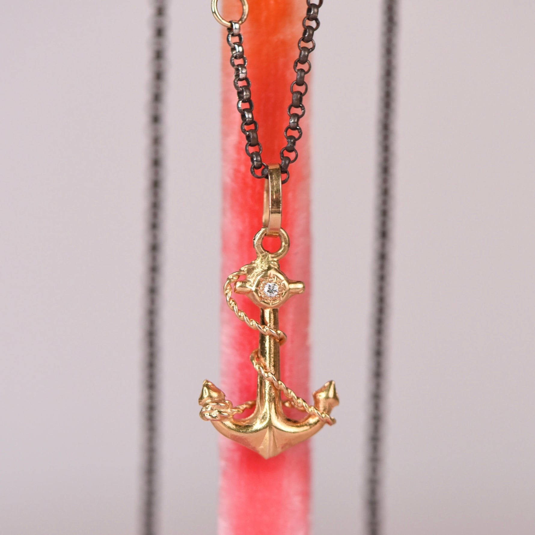 Vintage mid-century 18k yellow gold anchor and rope charm pendant with hand engraved star set white diamond hanging on an oxidized black rolo chain against a pink display stand, by Corkie Bolton Jewelry