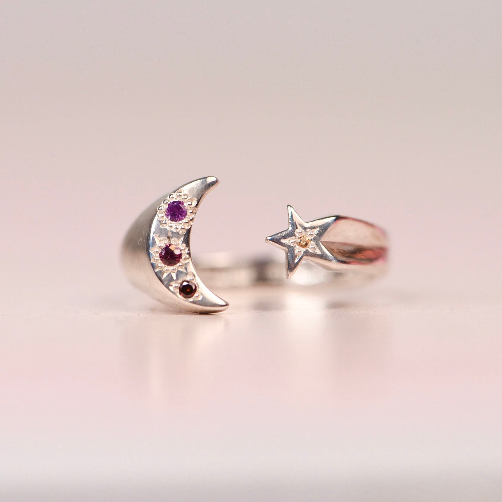 Vintage sterling silver open ring with crescent moon set with hand engraved purple pink and orange sapphires and orange diamond, and a star set with a yellow sapphire, displayed on a neutral surface by Corkie Bolton Jewelry