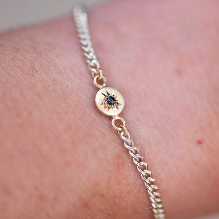Gold bracelet with a blue gemstone on a wrist against a neutral background