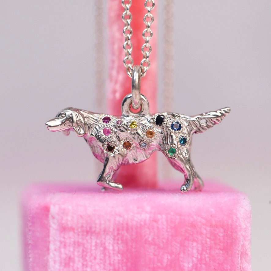 Vintage mid-century sterling silver golden retriever charm necklace hand engraved and flush set with a rainbow of sapphires and colored diamonds in pink, orange, teal, blue, green, yellow, and black, hanging on a silver cable chain against a pink velvet background.