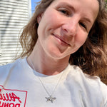 Jeweler Corkie Bolton wearing the vintage sterling silver golden retriever charm necklace on a silver cable chain, styled with a casual white graphic tee outdoors in natural light.