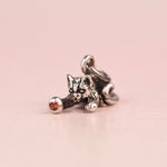Close up of a vintage sterling silver Jezlaine kitten charm playing with a ball set with an orange diamond, on a pink background