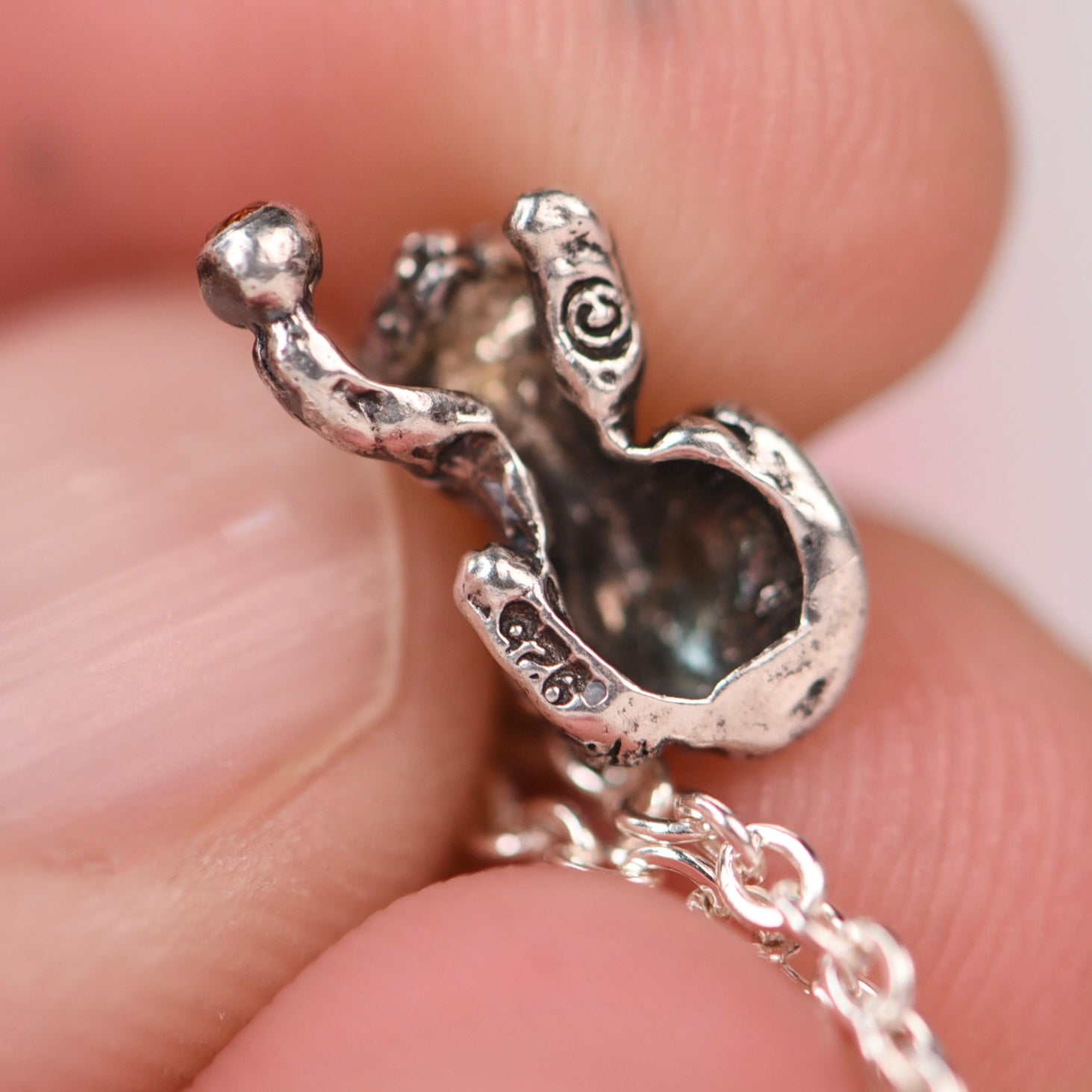 Underside view of a vintage sterling silver Jezlaine kitten charm held in fingers showing a hollow area and .925 and copyright stampings.