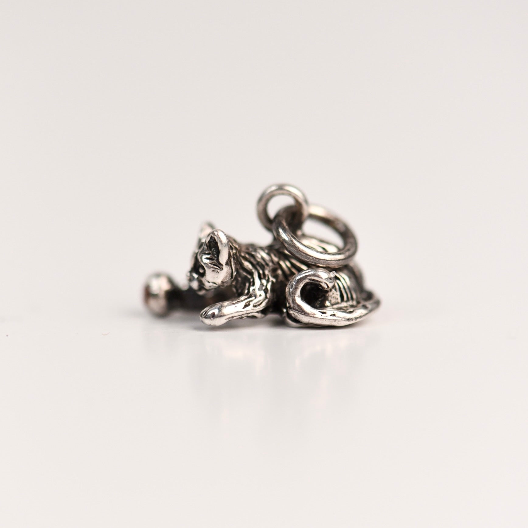 Side view of a vintage sterling silver Jezlaine kitten charm with detailed fur texture resting on a pink velvet surface