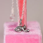Full length view of a vintage sterling silver Jezlaine kitten charm necklace hanging on a sterling silver cable chain against a pink velvet display stand