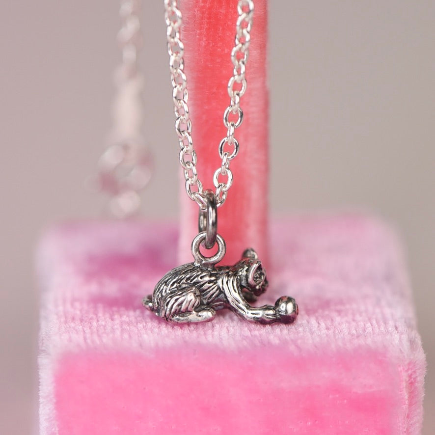 Full length view of a vintage sterling silver Jezlaine kitten charm necklace hanging on a sterling silver cable chain against a pink velvet display stand
