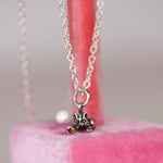 Vintage sterling silver Jezlaine kitten charm necklace with orange diamond set in the ball hanging on a pink velvet display stand