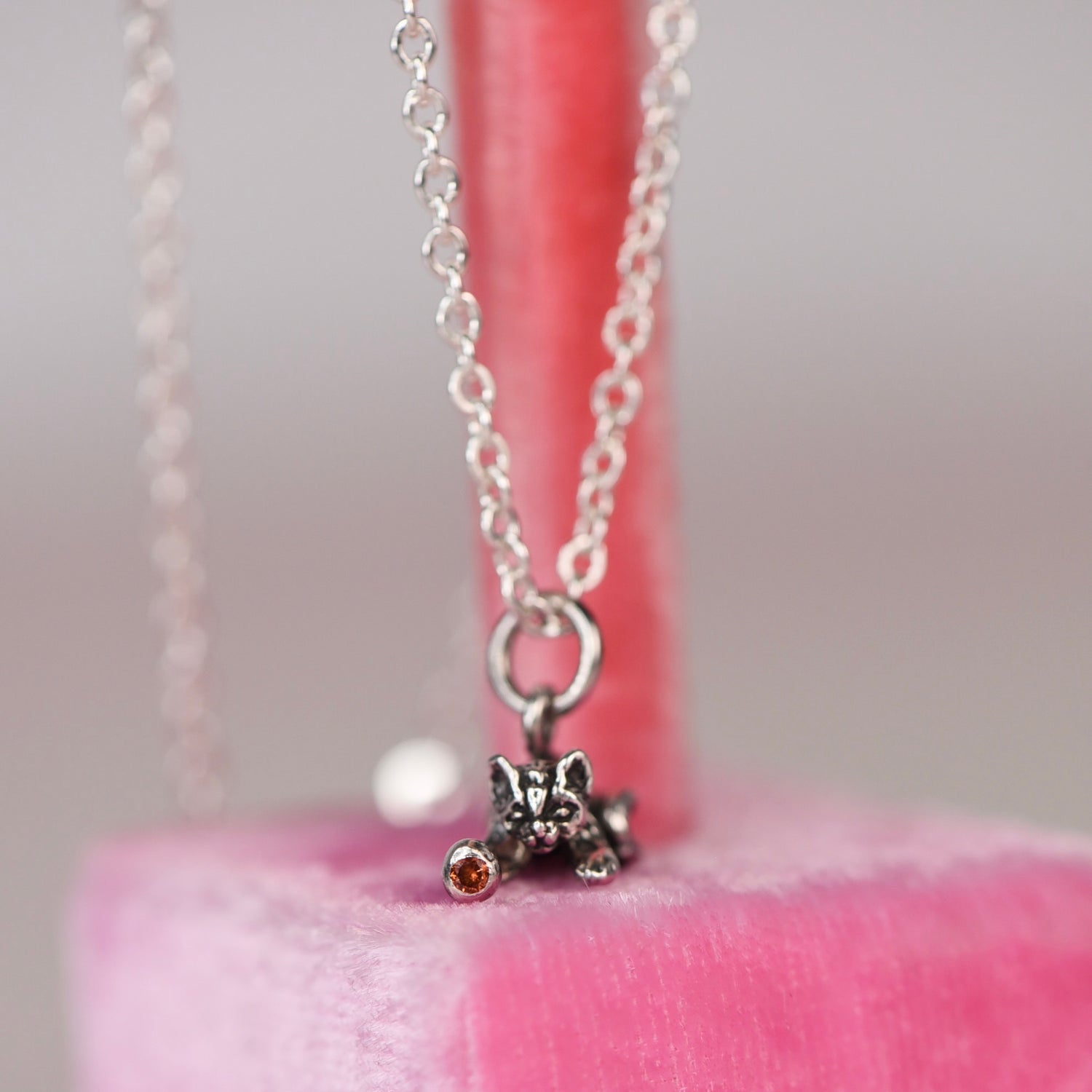 Vintage sterling silver Jezlaine kitten charm necklace with orange diamond set in the ball hanging on a pink velvet display stand
