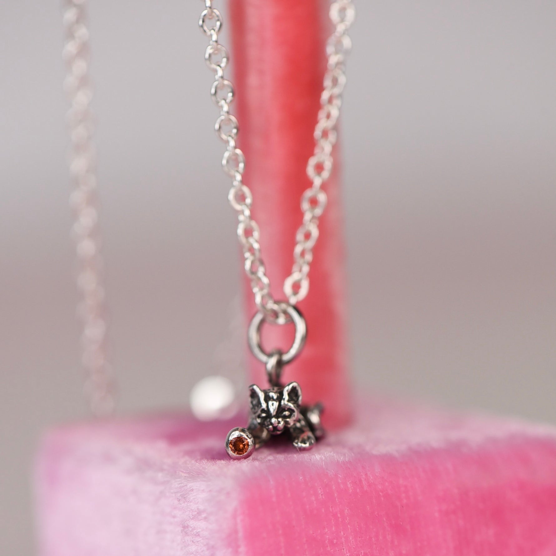 Vintage sterling silver Jezlaine kitten charm necklace with orange diamond set in the ball hanging on a pink velvet display stand