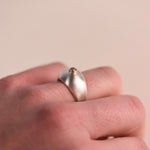 A chunky brushed sterling silver dome ring with a 14k yellow gold bezel set with a faceted salt and pepper diamond, worn on a hand against a soft neutral background, side angle view.