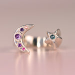 Vintage sterling silver open moon and star ring with hand engraved purple and pink sapphires on the crescent moon and a green rose-cut diamond on the star, displayed on a pink surface by Corkie Bolton Jewelry