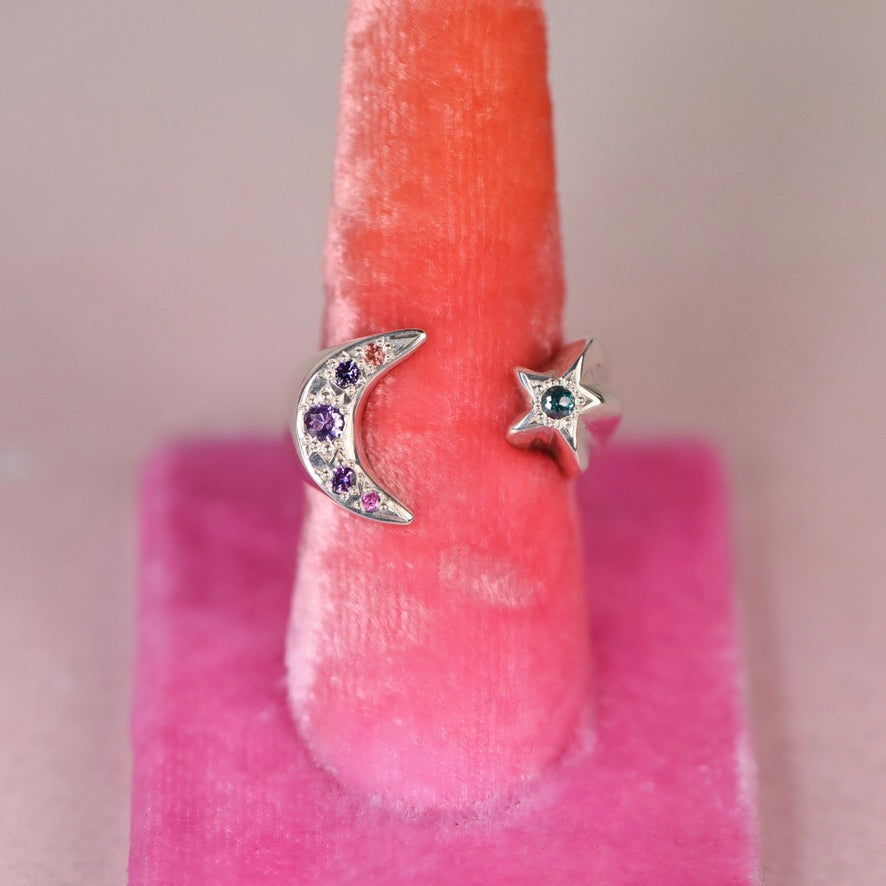 Vintage sterling silver open moon and star ring with hand engraved purple, orange and pink sapphires and green rose-cut diamond displayed on a pink velvet ring stand by Corkie Bolton Jewelry