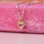Engraving details side angle of 14k Gold heart-shaped pendant with a pink ruby on a silver chain, displayed on a neon pink velvet display