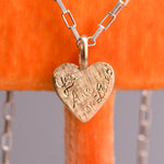 Heart-shaped pendant with engraved text on a chain against an orange background