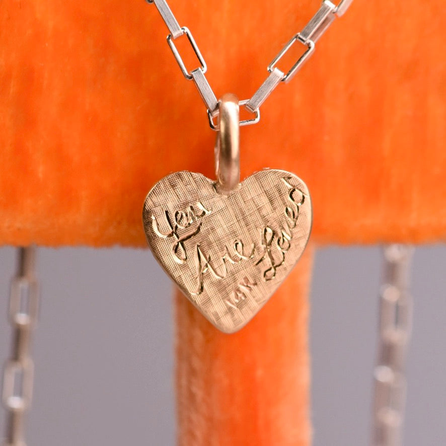 Heart-shaped pendant with engraved text on a chain against an orange background
