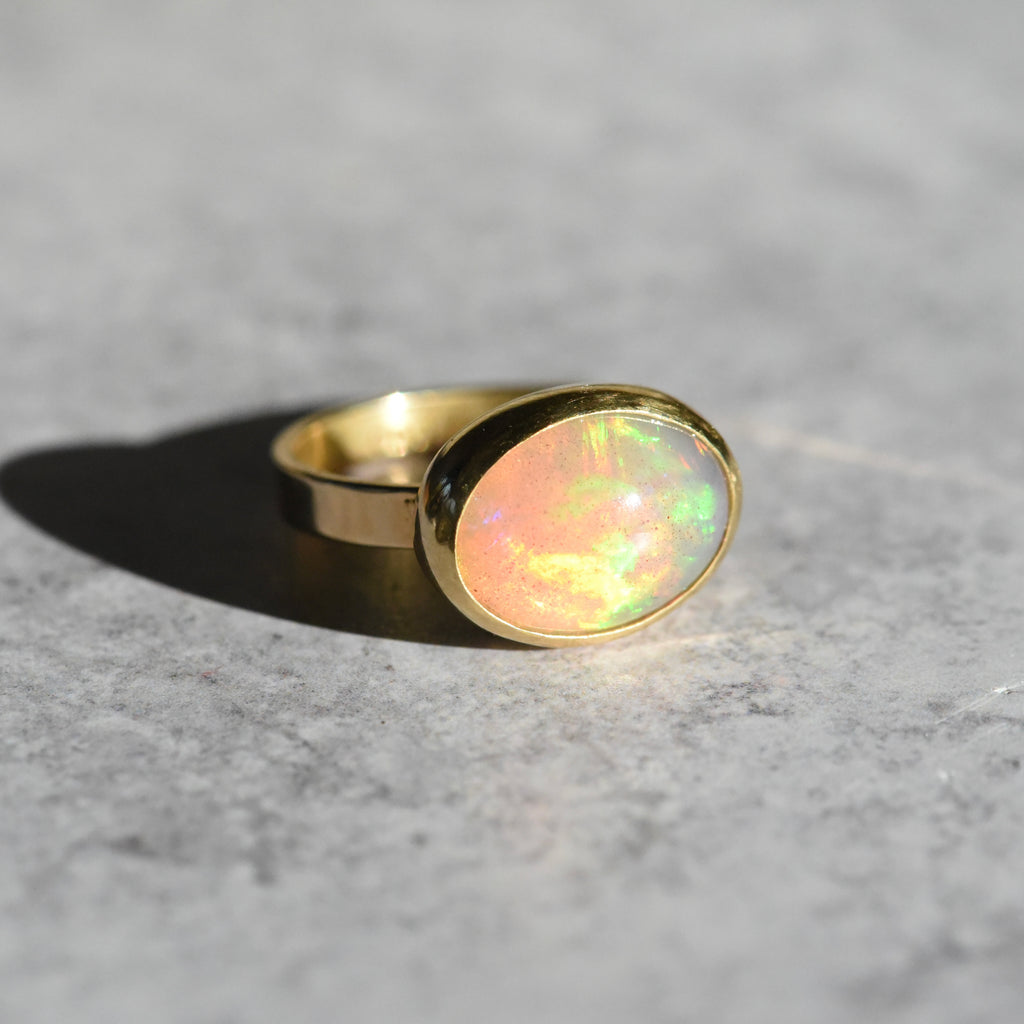 18k and 22k Gold Opal Ring on a white background, featuring a vibrant opal with flashes of blue and green, set in a rich yellow gold bezel.